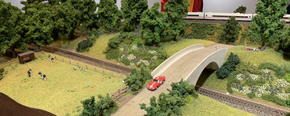 Ein Landschafts-Modul mit einem Porsche. Im Hintergrund ein ICE. Bild von der Ausstellung im Feuerwehr Museum Norderstedt (März-April 2025).
